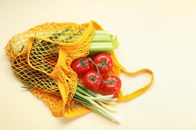 Photo of String bag with different vegetables on beige background