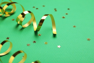 Photo of Shiny golden serpentine streamers and confetti on green background, closeup