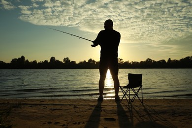 Fisherman with rod fishing at riverside at sunset, back view