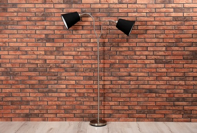 Photo of Stylish lamp on floor near brick wall