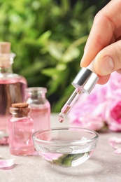 Photo of Woman dripping rose essential oil into bowl on table, closeup