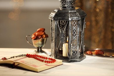 Photo of Arabic lantern, Quran, misbaha and dates on table against blurred lights