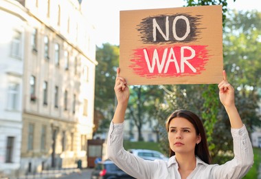 Photo of Sad woman holding poster with words No War on city street. Space for text