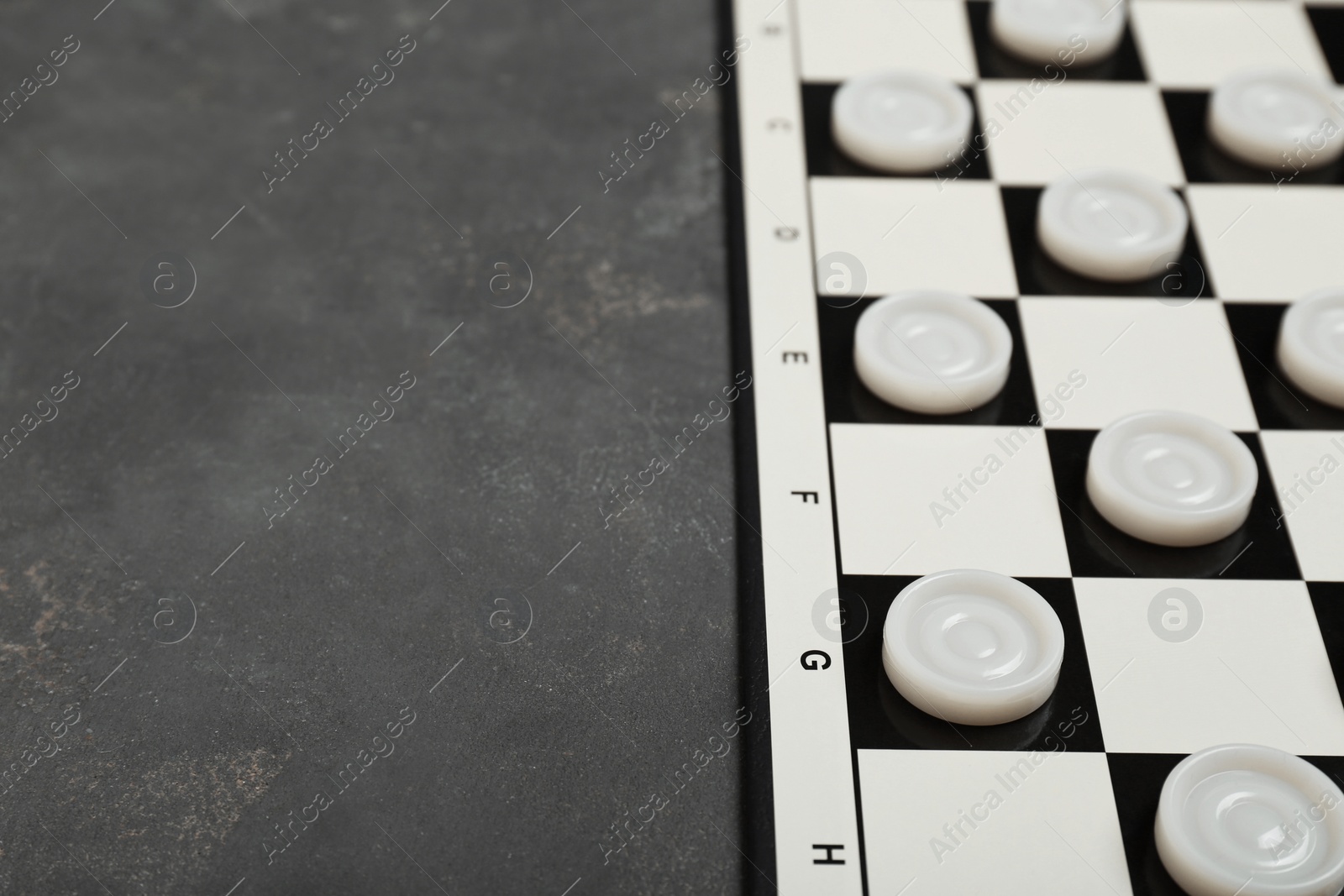 Photo of Checkerboard with game pieces on grey table, closeup. Space for text