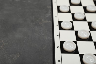 Photo of Checkerboard with game pieces on grey table, closeup. Space for text