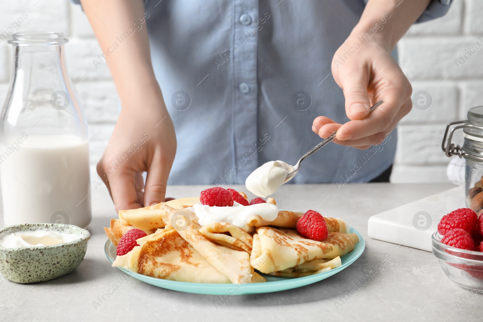 Photo of Woman adding sour cream to thin pancakes with berries at table