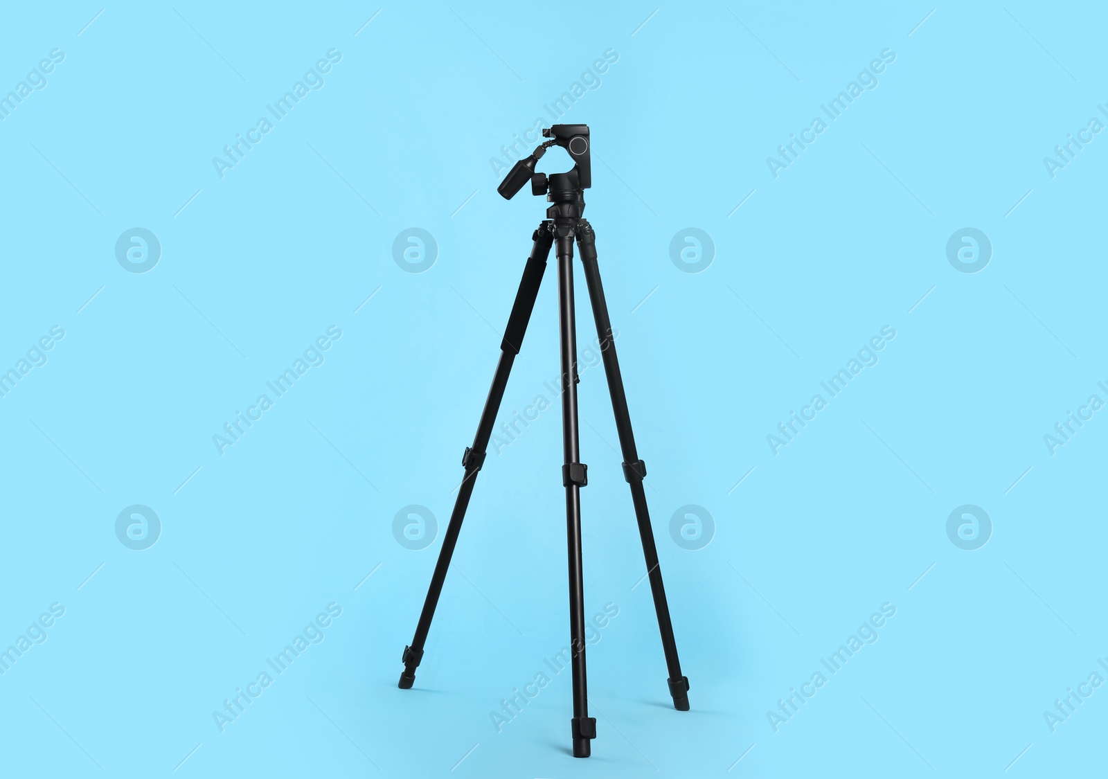 Photo of Modern tripod for camera on light blue background