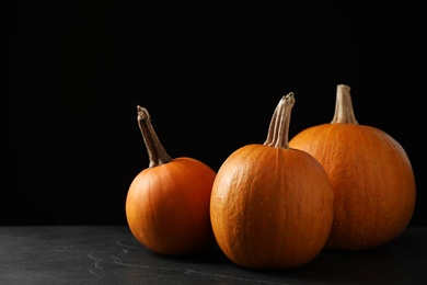 Photo of Ripe pumpkins on grey table against black background, space for text. Holiday decoration
