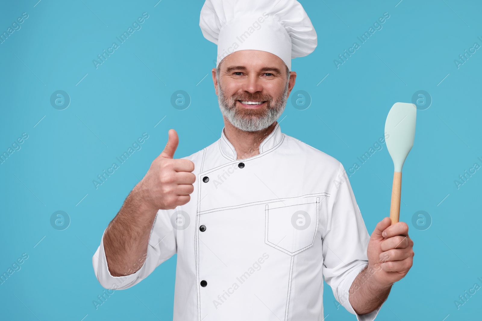 Photo of Happy chef in uniform with spatula showing thumbs up on light blue background