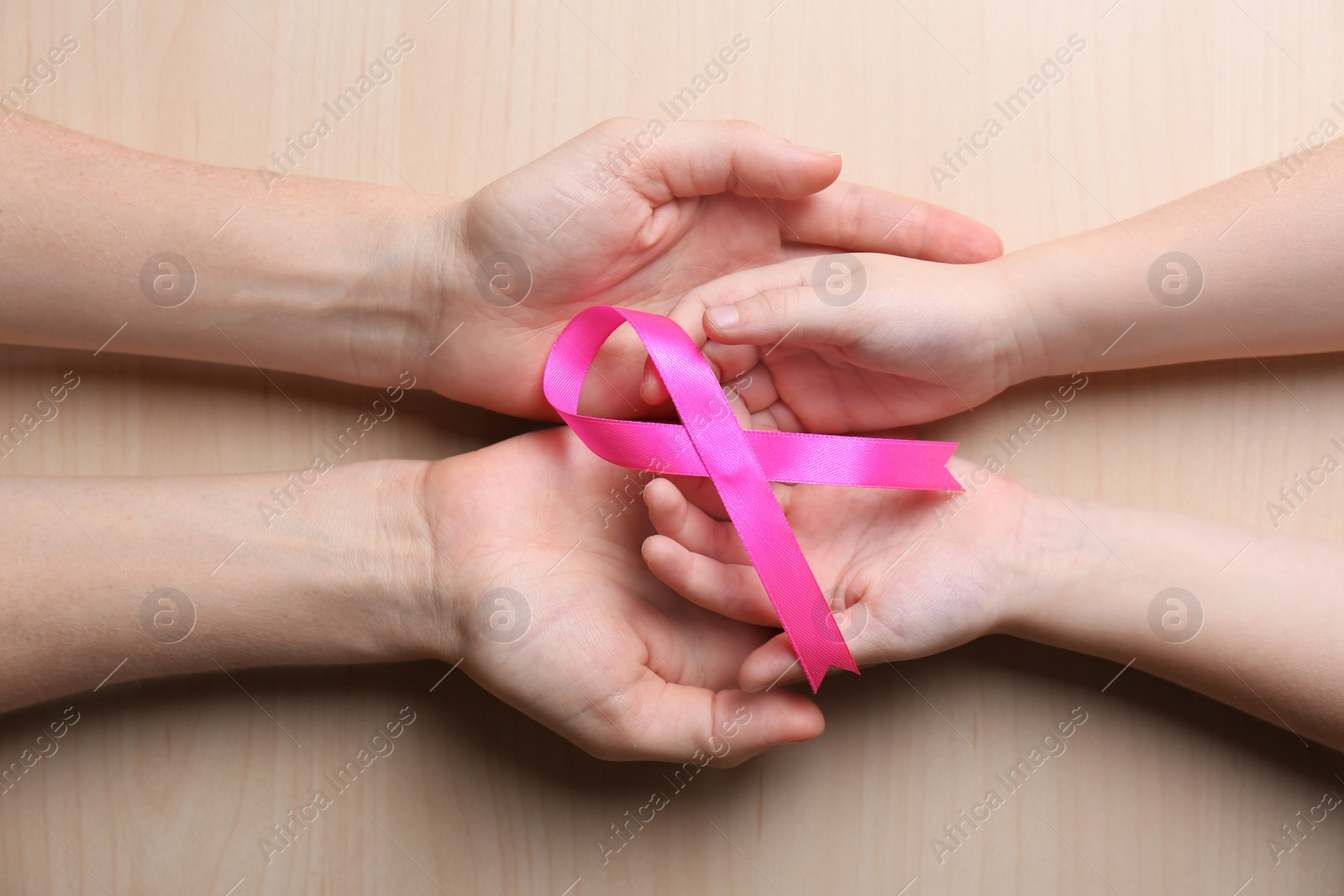 Photo of Woman and girl holding pink ribbon on wooden background, top view. Breast cancer awareness