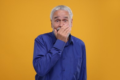 Photo of Portrait of embarrassed senior man covering mouth with hand on orange background