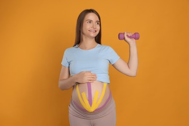 Photo of Pregnant woman with kinesio tapes on her belly doing exercises against orange background