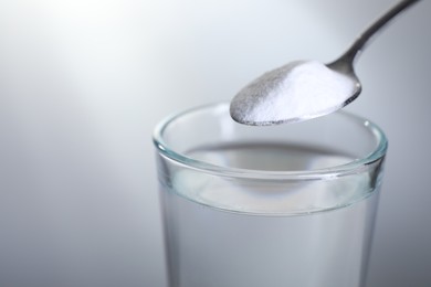 Spoon with baking soda over glass of water on light grey background, closeup. Space for text