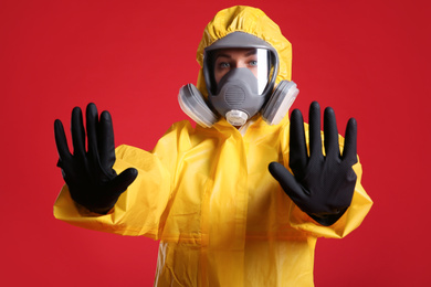 Woman in chemical protective suit making stop gesture on red background. Virus research