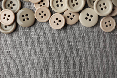 Photo of Many plastic sewing buttons on grey fabric, flat lay. Space for text