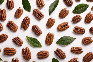 Photo of Delicious pecan nuts and green leaves on white background, flat lay