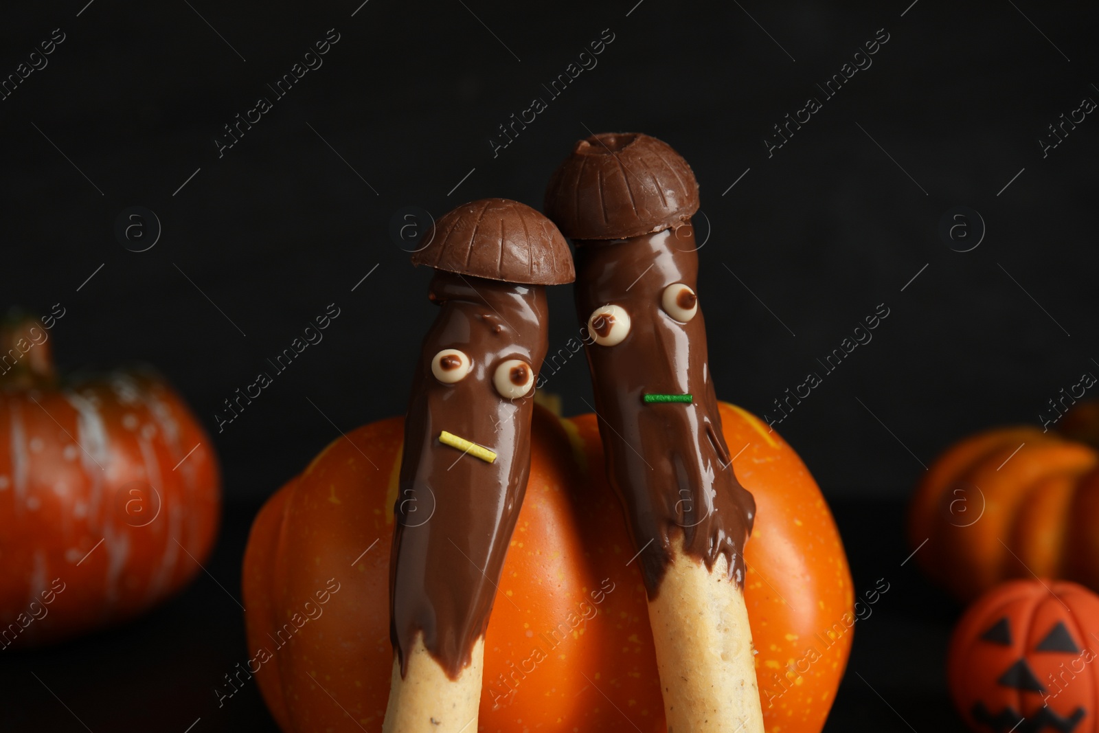 Photo of Delicious sticks with chocolate decorated as monsters on dark background, closeup. Halloween treat