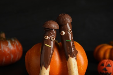 Photo of Delicious sticks with chocolate decorated as monsters on dark background, closeup. Halloween treat