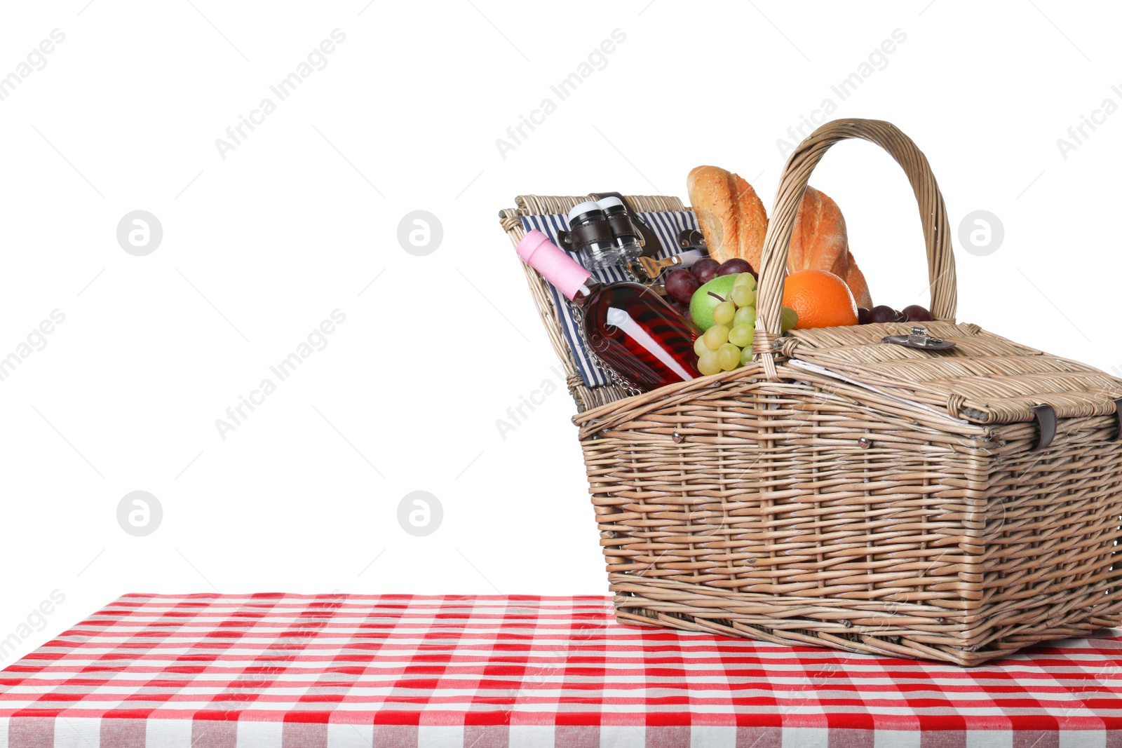 Photo of Wicker picnic basket with different products on checkered tablecloth against white background, space for text