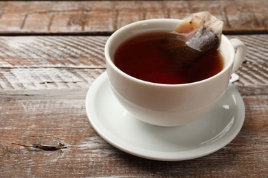 Photo of Tea bag in cup with hot drink on wooden rustic table, closeup. Space for text