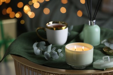 Photo of Beautiful burning candle, cup and eucalyptus branch on table indoors. Bokeh effect