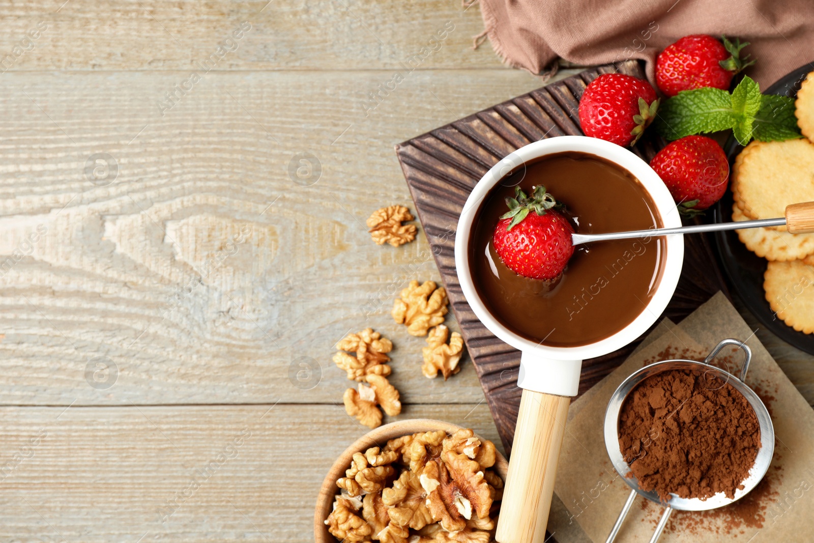 Photo of Dipping strawberry into fondue pot with milk chocolate on wooden table, flat lay. Space for text