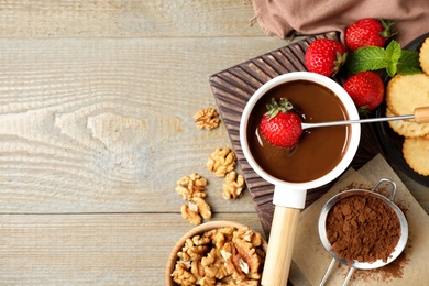 Photo of Dipping strawberry into fondue pot with milk chocolate on wooden table, flat lay. Space for text