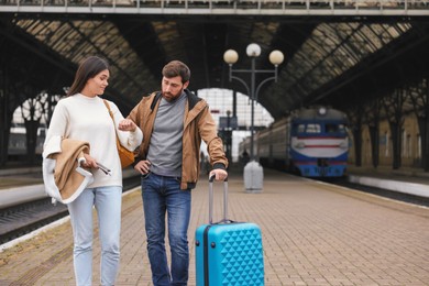Photo of Being late. Worried couple with suitcase waiting at train station, space for text