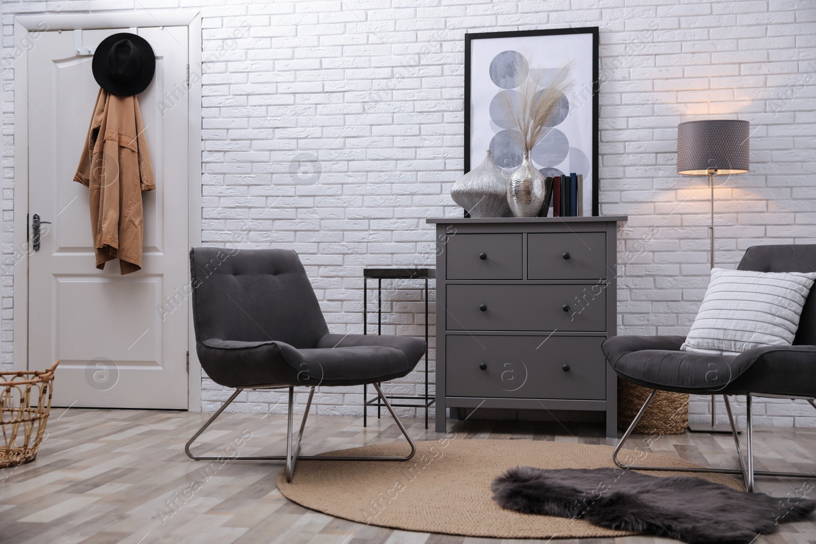 Photo of Stylish room interior with grey chest of drawers and chairs near white brick wall