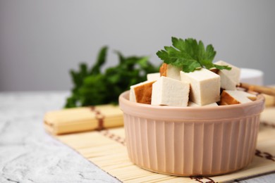 Photo of Bamboo mat with bowl of smoked tofu cubes and parsley on white textured table, closeup. Space for text