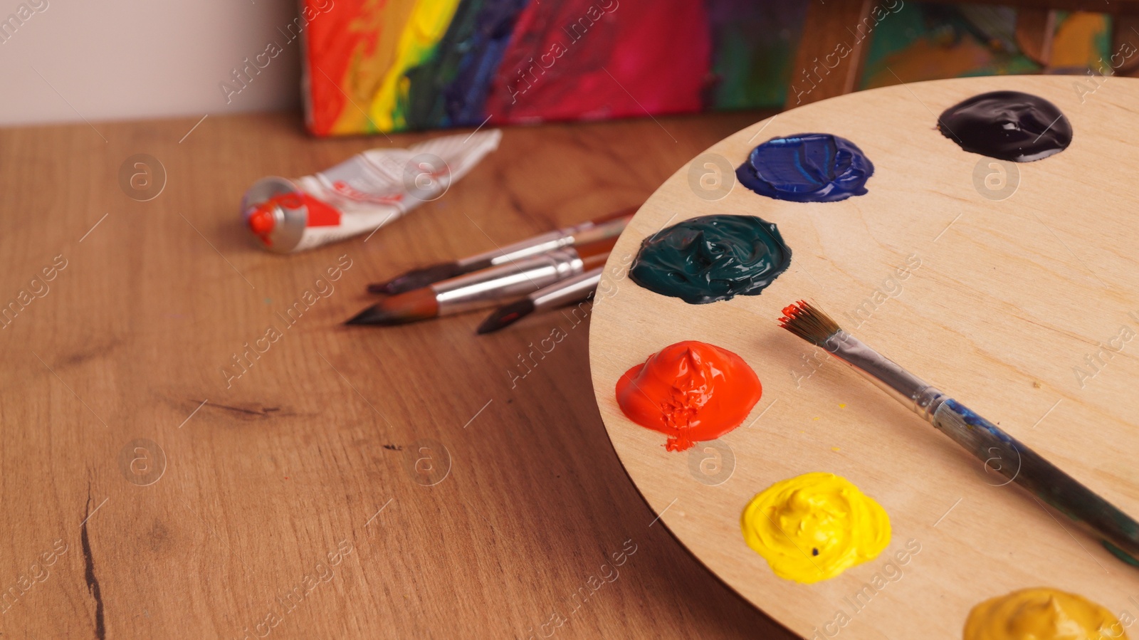 Photo of Artist's palette with samples of colorful paints and brush on wooden table. Space for text