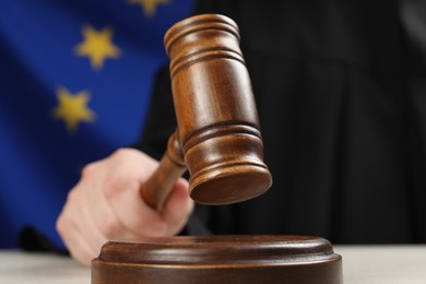 Photo of Judge with gavel at wooden table against flag of European Union, closeup