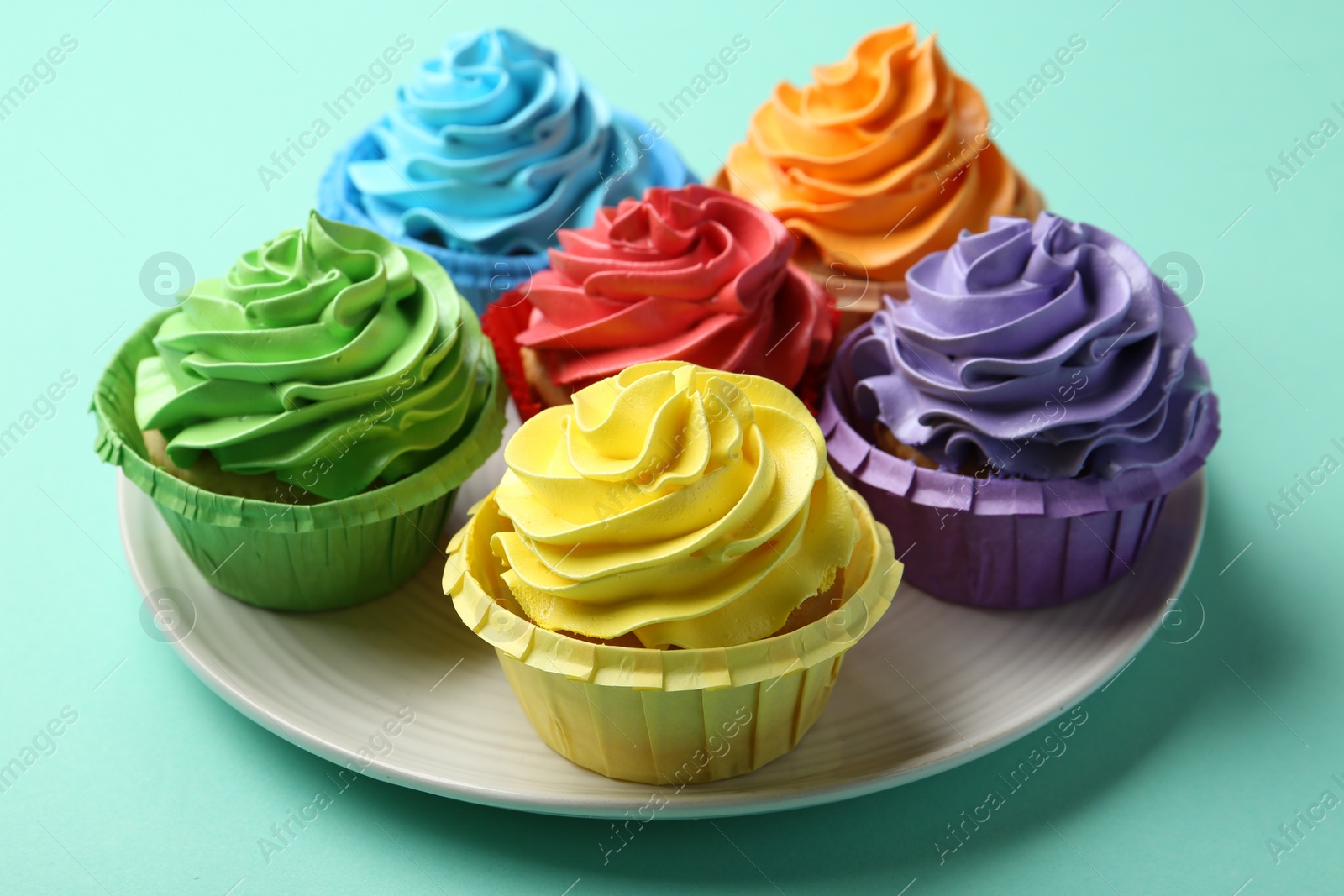 Photo of Plate with delicious bright cupcakes on turquoise background, closeup