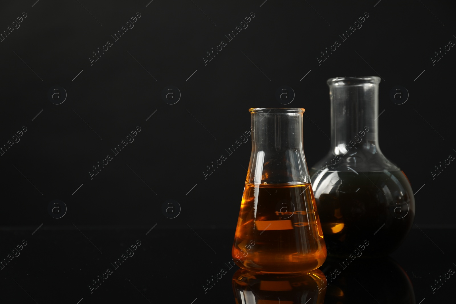 Photo of Glass flasks with different types of oil on black background, space for text