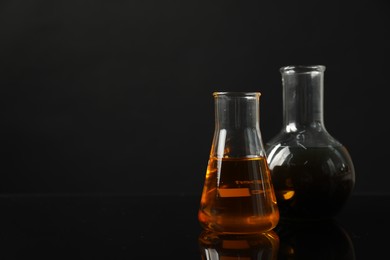 Glass flasks with different types of oil on black background, space for text