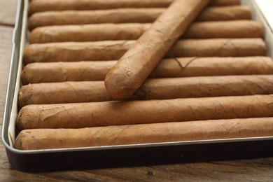 Photo of Many expensive cigars in box on wooden table, closeup