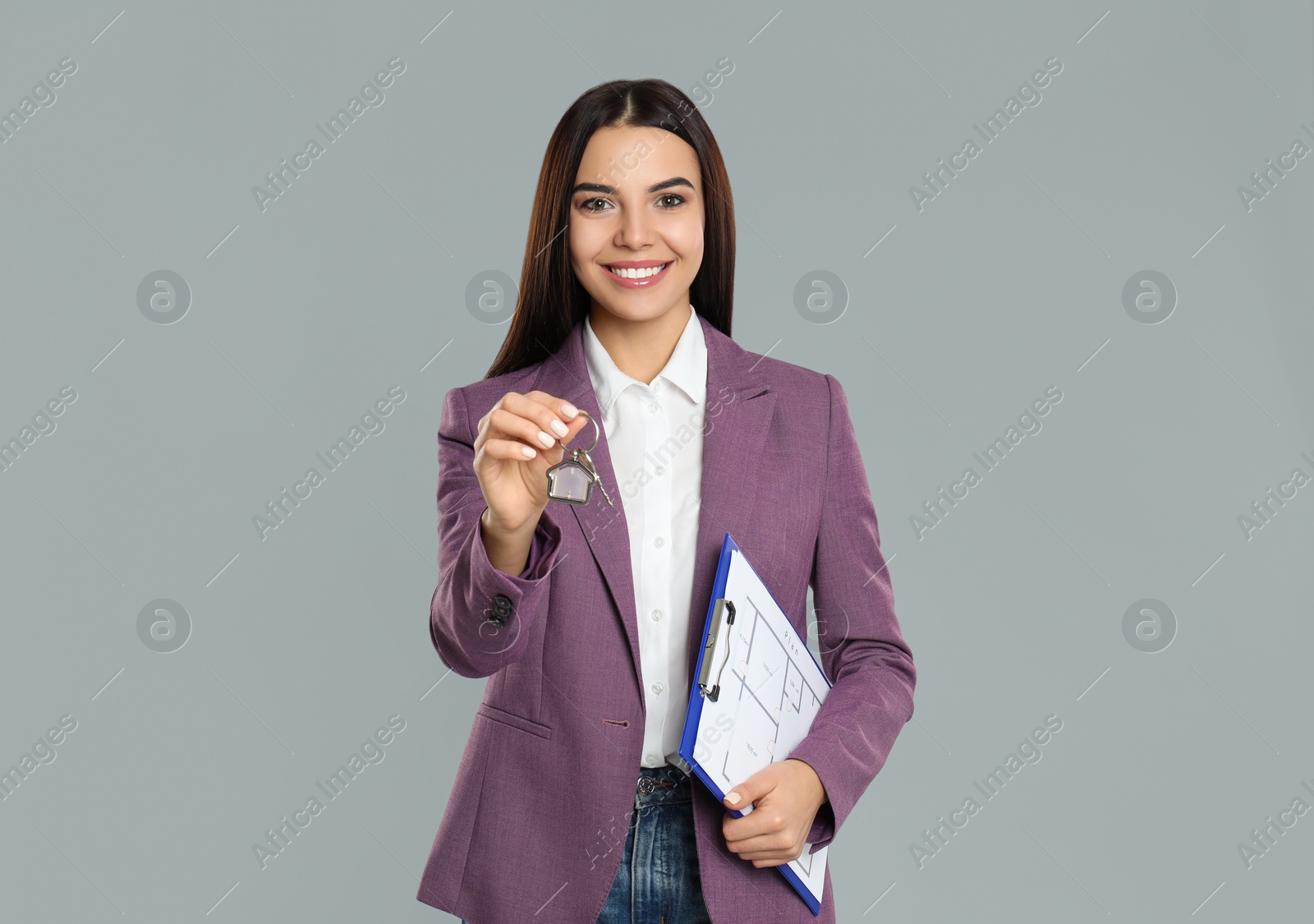 Photo of Female real estate agent with key and clipboard on grey background