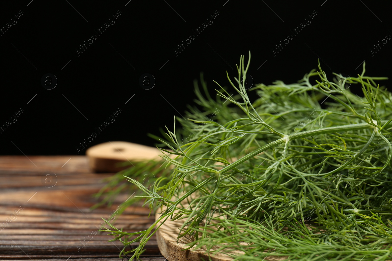 Photo of Board with fresh green dill on wooden table against black background, closeup. Space for text