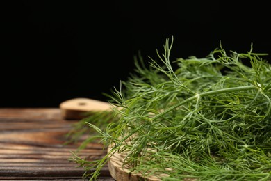 Board with fresh green dill on wooden table against black background, closeup. Space for text