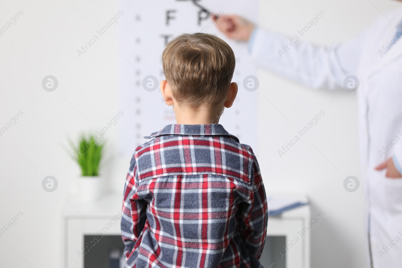 Photo of Ophthalmologist testing little boy's vision in clinic, back view