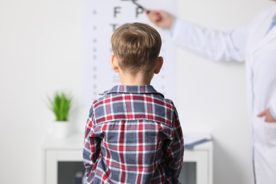 Photo of Ophthalmologist testing little boy's vision in clinic, back view