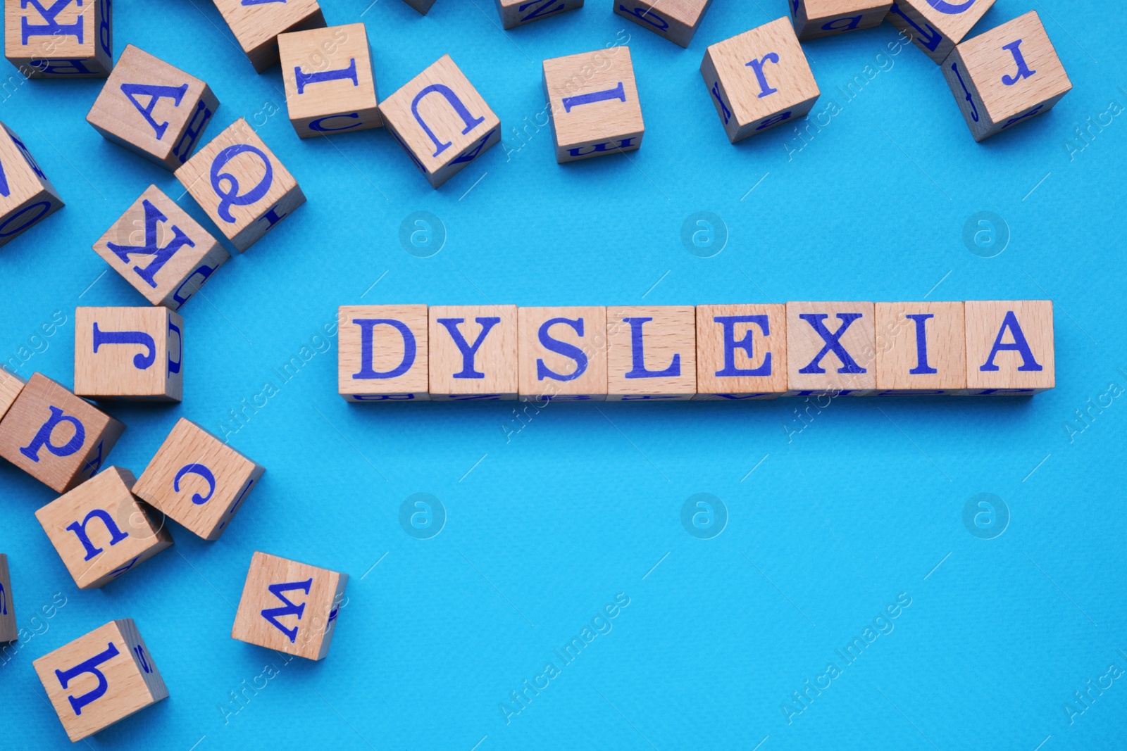 Photo of Wooden cubes with word Dyslexia on light blue background, flat lay. Space for text
