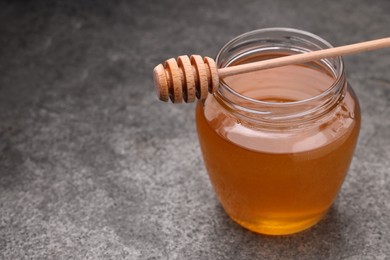 Sweet golden honey in jar and dipper on grey textured table, closeup. Space for text