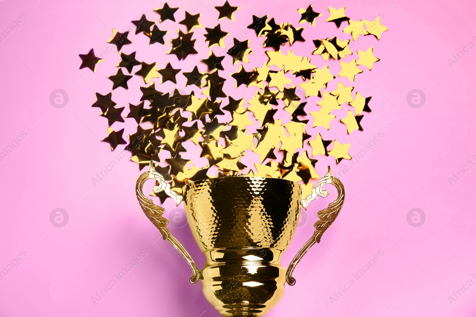 Photo of Golden trophy cup with confetti stars on pink background, flat lay