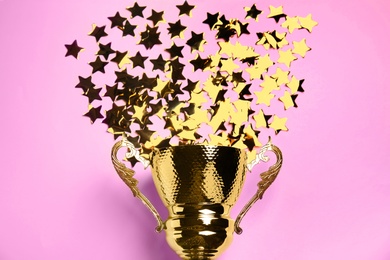 Photo of Golden trophy cup with confetti stars on pink background, flat lay