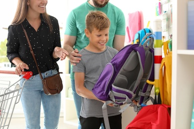 Photo of Little boy choosing school supplies with parents in stationery shop