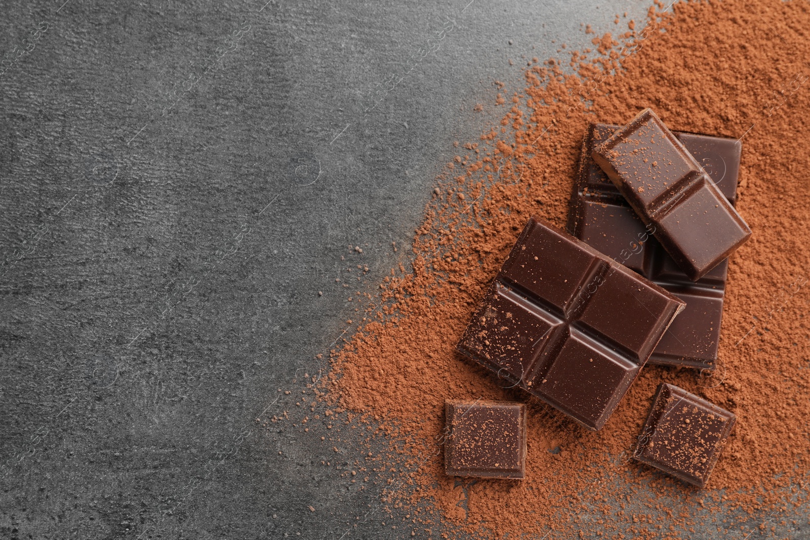 Photo of Delicious dark chocolate and cocoa powder on grey table, flat lay. Space for text