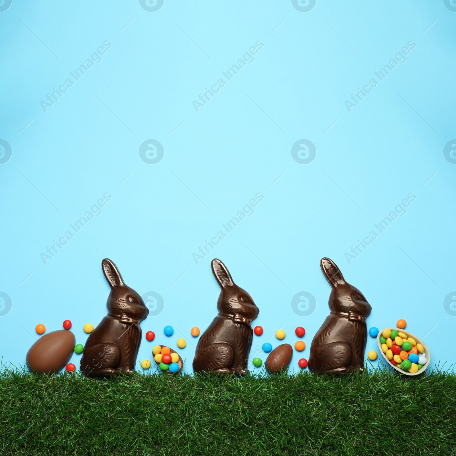 Photo of Chocolate Easter bunnies, eggs and candies with green grass on light blue background