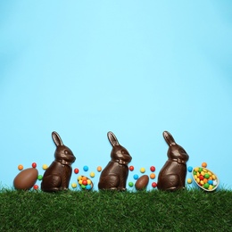 Photo of Chocolate Easter bunnies, eggs and candies with green grass on light blue background