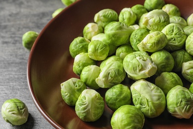 Photo of Plate of fresh Brussels sprouts on grey table, closeup